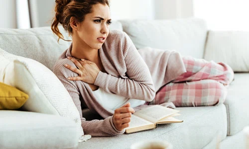 young woman having neckache while relaxing sofa reading book home jpg
