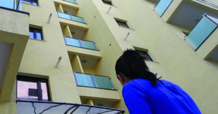 O tânără îmbrăcată cu bluză albastră privește un bloc nou
