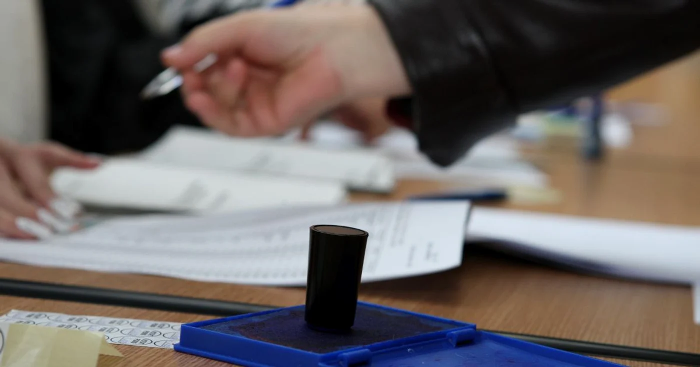 Un birou cu stampila de vot si buletine, unde semneaza o persoana ca a votat