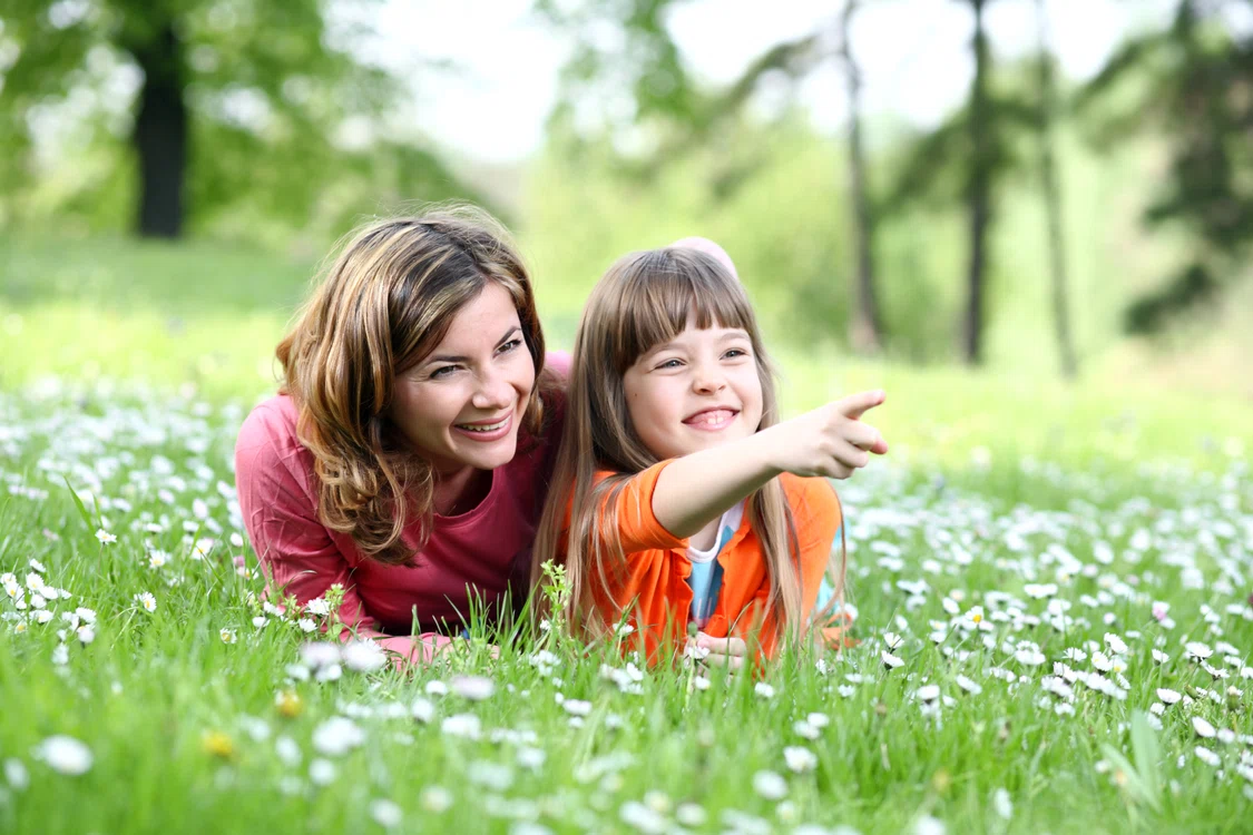 Femeie care sta in iarba cu fiica ei si se bucura de natura