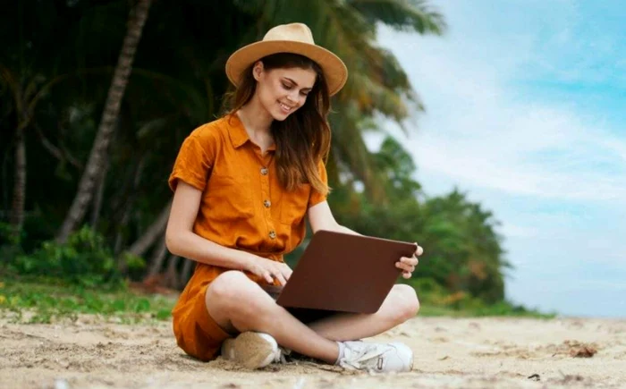 Tânără care scrie la un laptop pe o plajă din Portugalia