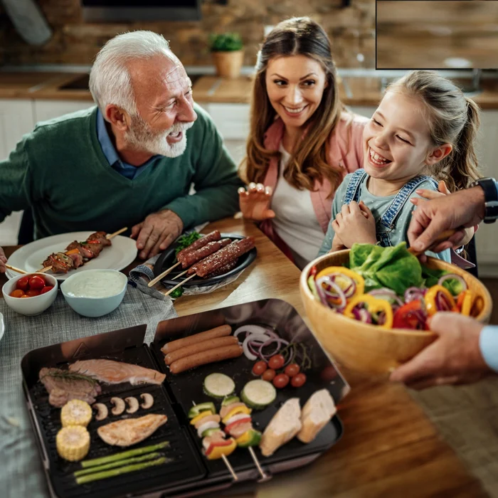 Familie fericită strânsă la masă în jurul unui grătar electric ce prepară alimente diverse Foto eMAG