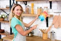 smiling woman looking camera while dusting kitchen jpg