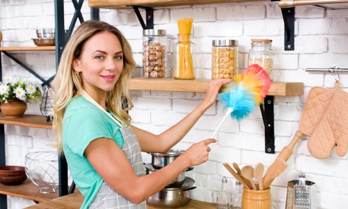 smiling woman looking camera while dusting kitchen jpg