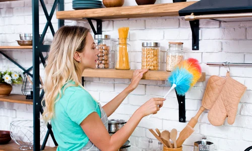 pretty woman cleaning kitchen shelf with soft feather duster jpg