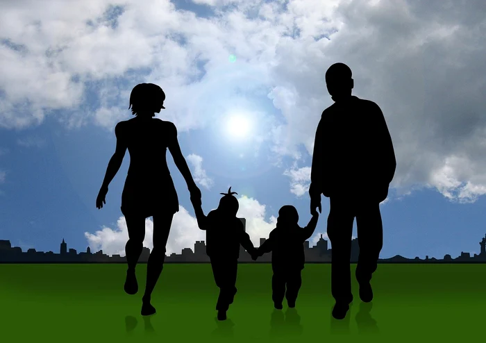 O familie cu doi copii alergând pe o pajiște la marginea orașului