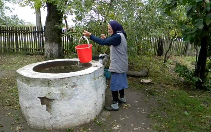 Bătrâna scoate cu greu apa din fântână