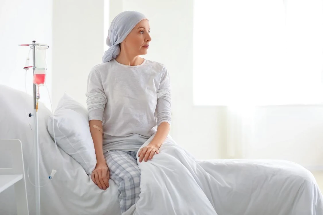 Femeie pe marginea unui pat de spital, în timp ce i se face o perfuzie