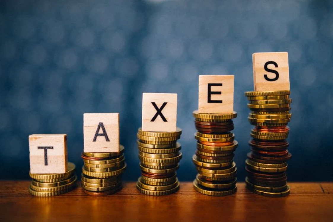 Fișicuri de monede în ordine crescătoare peste care sunt puse litere care formează cuvântul Taxes