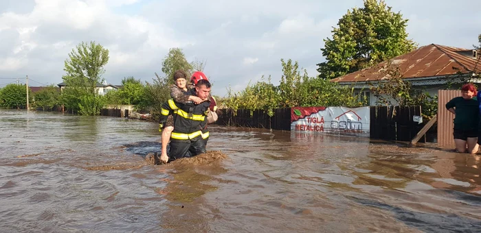Un pompier cară în spate o bătrânică prin apa mare care a inundat satul