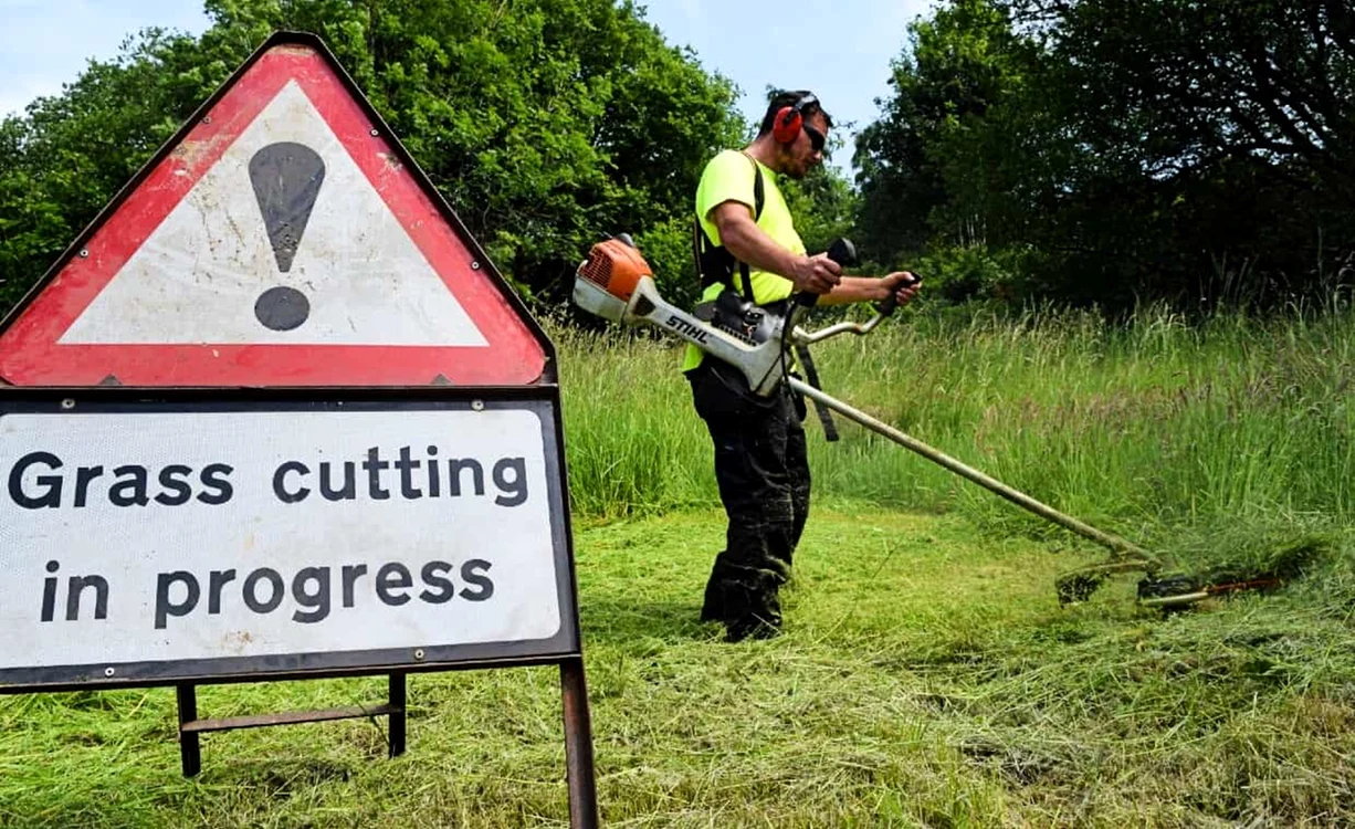 Bărbat tăind iarba pe o suprafață mare cu semn de avertizare Grass Cutting in Progress F:hovtraining