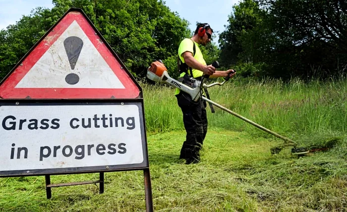 Bărbat tăind iarba pe o suprafață mare cu semn de avertizare Grass Cutting in Progress F:hovtraining
