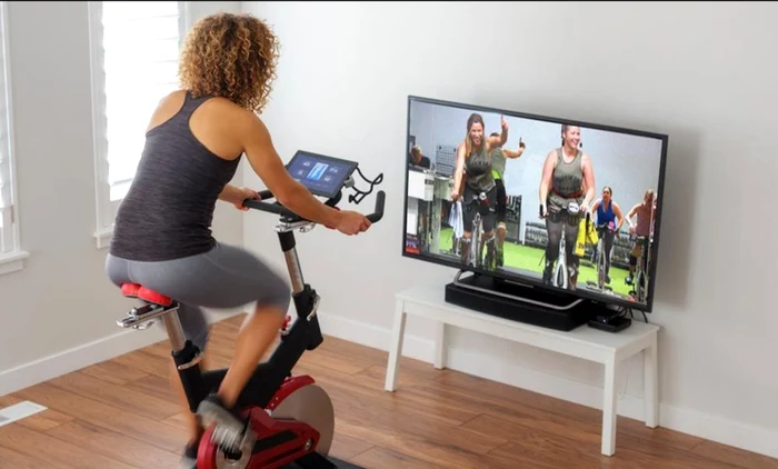 Femeie care face fitness digital în confortul casei pe o bicicletă Foto studiosweatondemand com