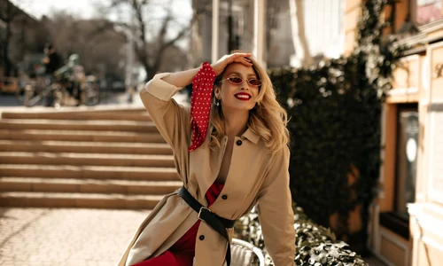 happy joyful blonde curly woman silk bright dress colorful sunglasses beige trench coat sits table smiles outside jpg