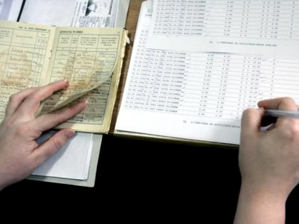 O angajată transcrie datele din cartea de muncă într-un registru