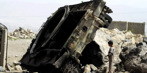 Un baiat stă langa un vehicul blindat distrus pe un drum din provincia Omran Yemen FOTO Reuters