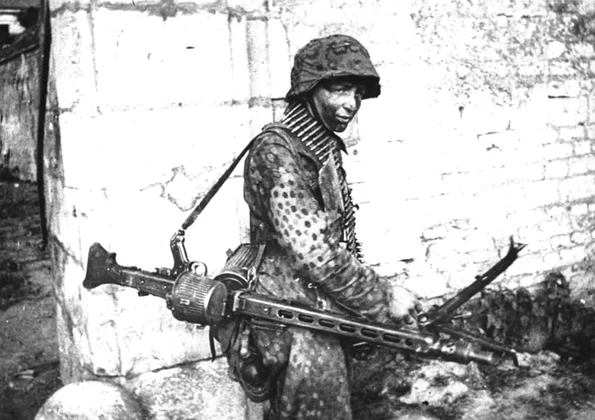 Soldat german purtând o mitralieră MG-42, pe frontul din Franța, în 1944 (© Das Bundesarchiv Bild 146-1983-109-14A)