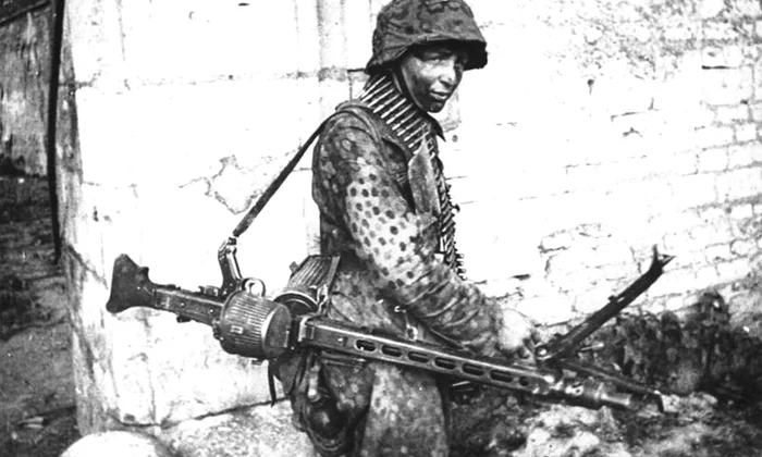 Soldat german purtând o mitralieră MG-42, pe frontul din Franța, în 1944 (© Das Bundesarchiv Bild 146-1983-109-14A)
