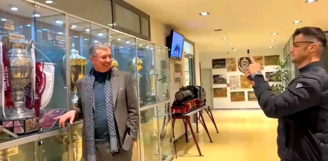 Eugen Voicu, pozat de Andrei Nicolescu în fața vitrinei cu trofee a lui CFR Cluj. Captură Antena 1