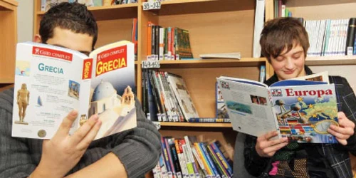 Claudiu (dreapta) vine la centrul de consiliere pentru copiii cu părinţii plecaţi ca să citească despre locul unde se află mama sa