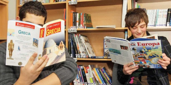 Claudiu (dreapta) vine la centrul de consiliere pentru copiii cu părinţii plecaţi ca să citească despre locul unde se află mama sa