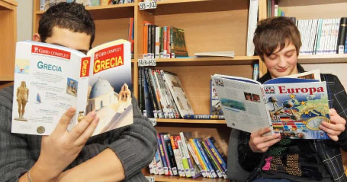 Claudiu (dreapta) vine la centrul de consiliere pentru copiii cu părinţii plecaţi ca să citească despre locul unde se află mama sa