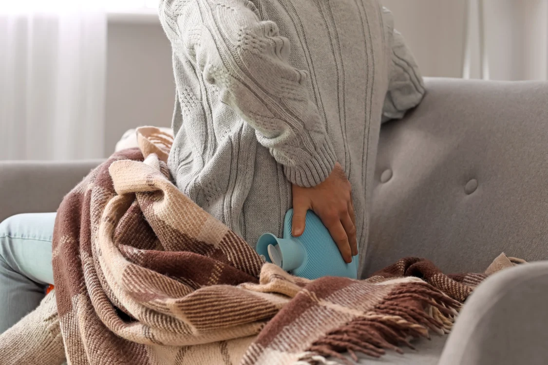 Persoană care-și ameliorează durerile lombare cu o sticlă cu apă caldă Foto Shutterstock