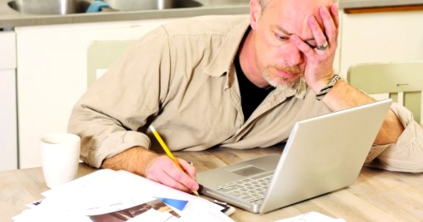 Un bărbat se uită îngrijorat la graficele economico-financiare de pe laptop