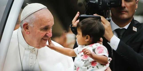 Un copil din mulţime îl atinge pe faţă pe Papa Francisc care s-a oprit în drumul către slujba de duminică în parcul Benjamin Franklin din Philadelphia FOTO AP