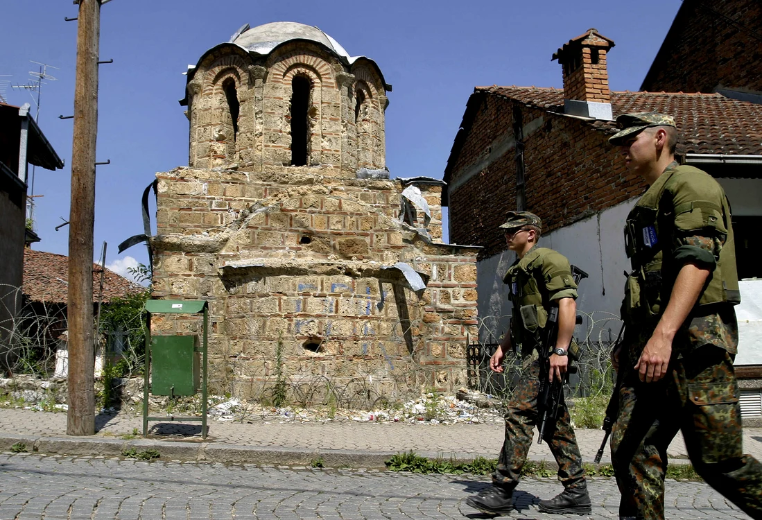 Germani din trupele KFOR patrulând în 2005,  în apropierea unei biserici ortodoxe devastate cu un an mai devreme în oraşul Prizren