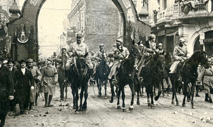 Foto sus: Trecerea familiei regale și a generalului Berthelot pe sub Arcul de Triumf ridicat pe Calea Victoriei, la intrarea în Piața Palatului Regal, la 18 Noiembrie/1 Decembrie 1918 (© Colecția Muzeului Militar Naţional „Regele Ferdinand I”)