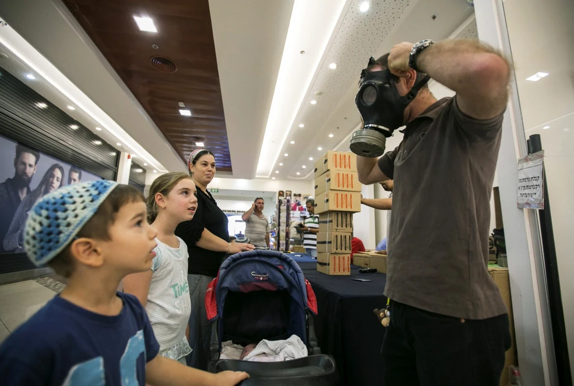 Un israelian le arată copiilor cum să îşi pună masca de gaze în cazul unui atac chimic FOTO Reuters