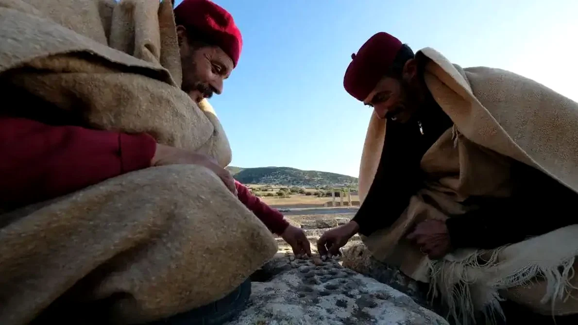 Locuitori din Tolmeita, îmbrăcați în costume tradiționale, joacă un joc pe zidurile Pieței Cisternei din Ptolemais (© Piotr Jaworski)