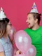 surprised young couple wearing party hat looks each other standing with helium balloons isolated pink wall jpg