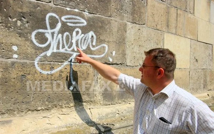 Administratorul bisericii arată un graffiti mâzgălit pe zidul lăcaşului FOTO: Mediafax