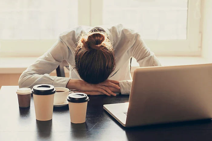 O femeie care doarme la birou având în față mai multe pahare cu cafea Sursă imagine Istock