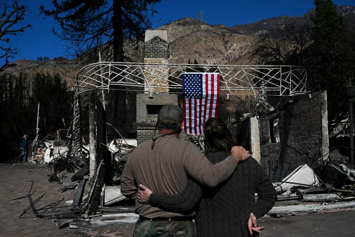 Cuplu în fața unui case arse pe care este atârnat steagul american, ianuarie 2025 - GettyImages