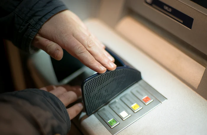 Un bărbat introduce codul PIN la ATM, acoperind cifrele cu cealaltă mână