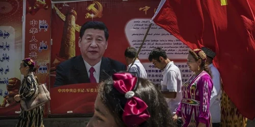 n grup de persoane cu steagul Partidului Comunist Chinez în faţa unui afiş cu preşedintele Xi Jinping in Kashgar