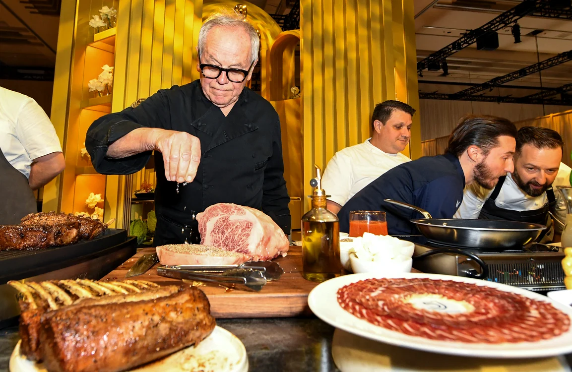 Bucătarul Wolfgang Puck pune condimente pe o bucată de carne. Marite 2024