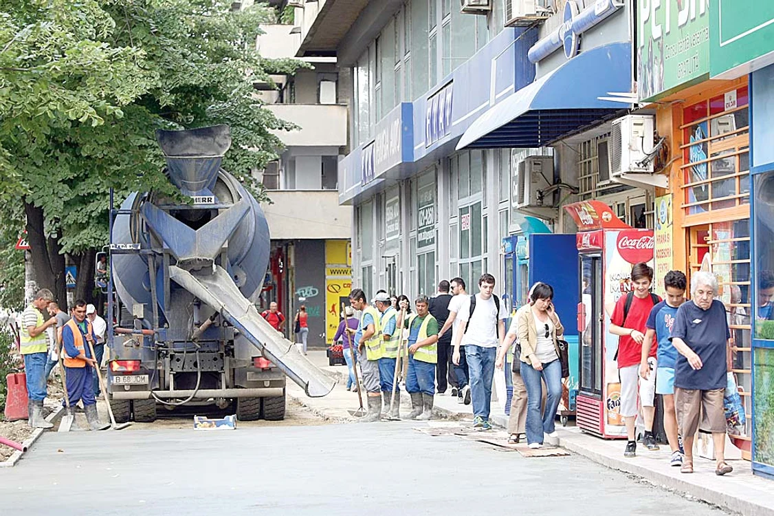 Muncitorii toarnă  beton pe trotuare,  iar pietonii fac  slalom printre utilaje