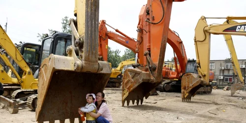 O mama cu copilul sta în umbra unei cuve de excavator la o staţie de întreţinere maşini în Shanghai FOTO Reuters