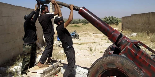 Luptători din Armata Siriană Liberă se pregătesc să lanseze un proiectil de artilerie în Idlib