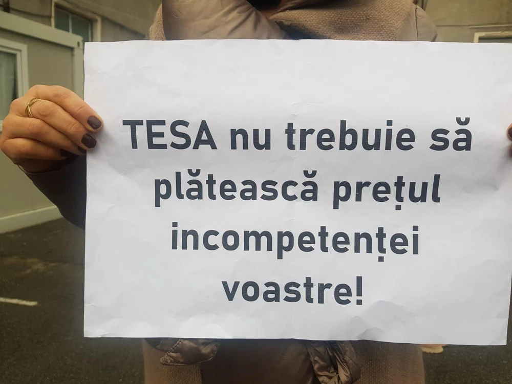 O femeie ține în mână o hârtie pe care scrie „TESA nu trebuie să plătească prețul incompetenței”