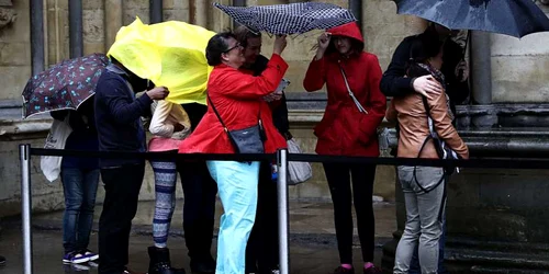 Oamenii care stau la rând se adăpostesc sub o folie de plastic şi umbrele în timp ce aşteaptă să intre în Westminster Abbey la Londra Anglia FOTO Guliver/Getty Images