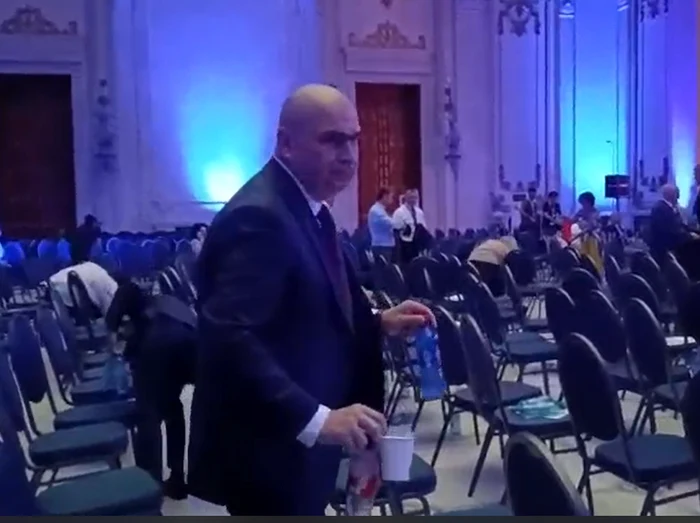 Premierul Ilie Bolojan strânge gunoaiele din sală FOTO: Captura video