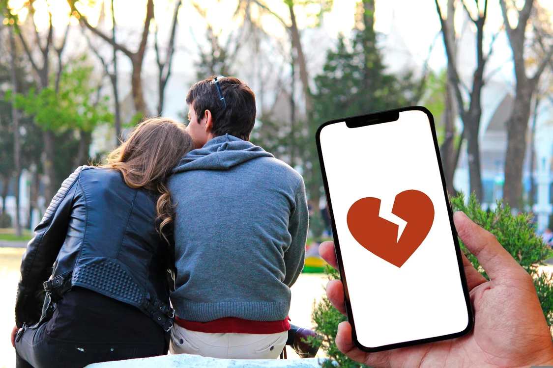 Doi tineri indragostiti in parc si un telefon pe care apare o inima franta