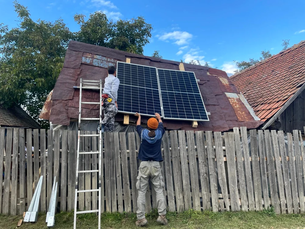 Doi bărbați montează panouri fotovoltaice pe un acoperiș