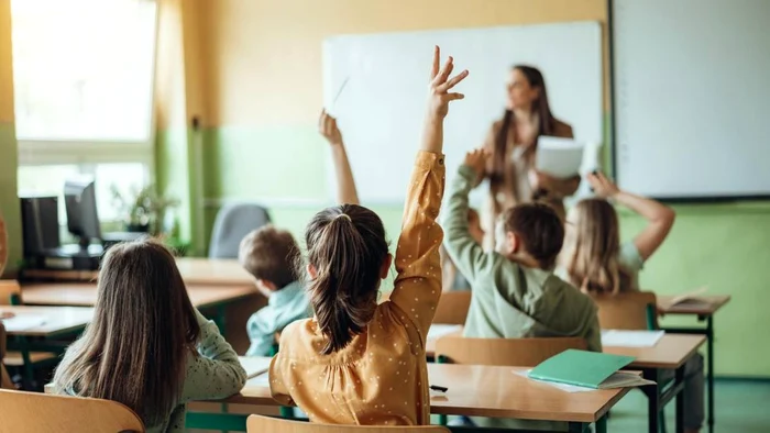 Elevi în timpul orei de curs cu mâna ridicată