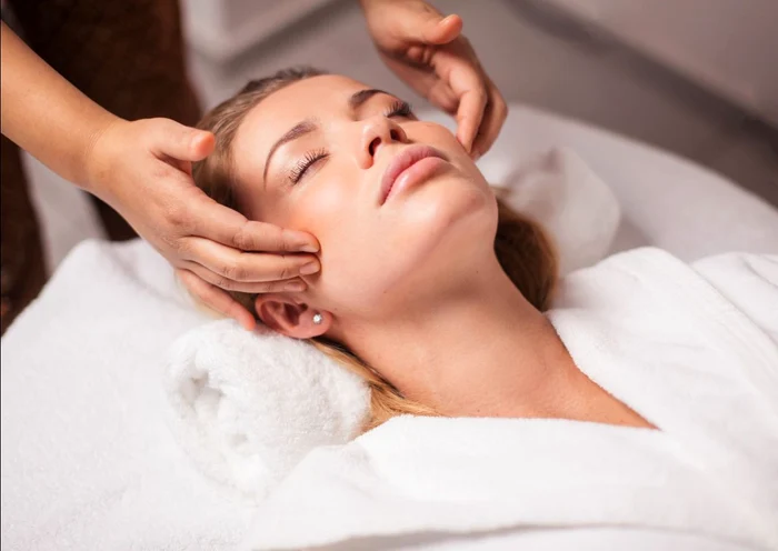 Femeie întinsă pe un pat la un salon, în timp ce i se face un masaj facial